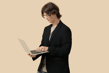 Male programmer in eyeglasses working with modern laptop on beige background