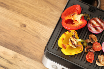 Modern electric grill with tasty vegetables on wooden table