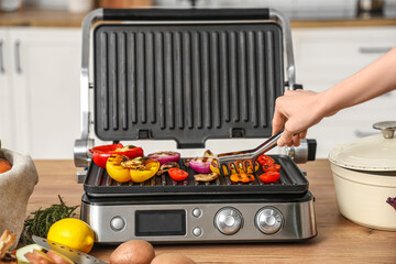 Young woman cooking tasty vegetables on modern electric grill in kitchen