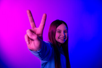 Wall Mural - Photo of adorable lovely small girl wear hoodie showing you v-sign empty space isolated magenta blue color background