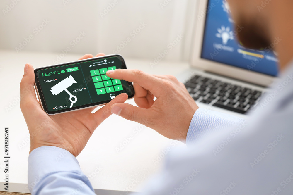 Young man using mobile phone with smart home security system application at table in room, closeup