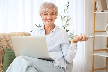 Canvas Print - Mature woman with laptop and mobile phone sitting on sofa at home