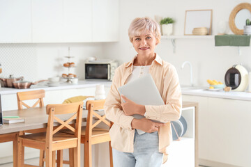 Poster - Mature woman with laptop in kitchen