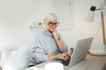 Wall Mural - Blonde caucasian woman working on her laptop from her home office