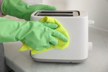 Wall Mural - Woman wiping toaster with rag at countertop in kitchen, closeup