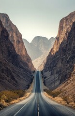 A straight highway leading through a mountain pass, with towering peaks on either side and a clear sky above