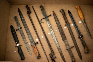 A collection of old knives and swords are displayed in a box