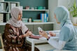 © AnnaStills - Female doctor in hijab engaging in conversation with patient in office environment, both focused on the discussion, surrounded by medical tools and office supplies