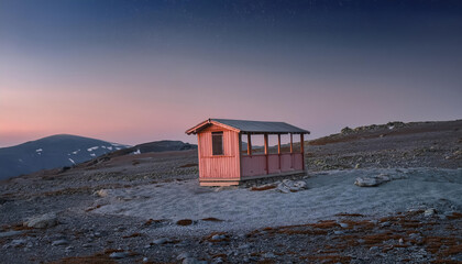 Photograph of a small pink wooden hut on top of a mountain, with a clear sky at dusk. Closed Kiosk outside.