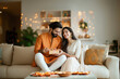 © PRASANNAPIX - A handsome young Indian man in traditional wear giving a gift to his beautiful wife who wearing sari, sitting on a sofa. Both are smiling and happy