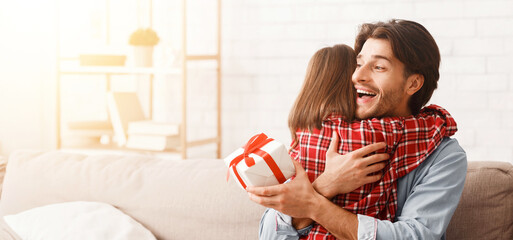 Wall Mural - Emotional young father hugging his little daughter, holding gift box at home, free space