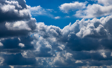 Dramatic cloudscape on a sunny day with dark and bright white clouds, hidden sun and blue sky. Wide angle shot on a day with changing weather in Germany after rain shower. Monochrome background.