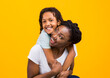 © Prostock-studio - Togetherness Concept. African daughter hugging her mum from the back, showing her love, yellow studio wall