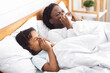 © Prostock-studio - Respiratory Disease. Black mom and daughter sneezing, blowing noses on paper napkins in bed