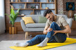 © Tetiana - Contorted in pain, a young Indian man sits on an exercise mat at home and holds his leg with his hands, injured and sprained while exercising