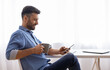 © Prostock-studio - Break In Work. Relaxed Male Freelancer Using Smartphone And Drinking Coffee While Sitting At Desk At Home Office, Browsing Internet Or Social Networks, Enjoying Remote Job, Side View With Copy Space