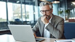 © halo - A photograph of an attractive middle-aged man in glasses, sitting at his desk with papers and a laptop, contemplating the marketing plan for his company.