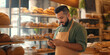 © Oleksandr - Young Hispanic man with a beard uses a mobile phone in a bakery interior with shelves of bread in the background