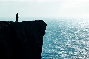 Wall Mural - A solitary figure stands on a cliff overlooking a vast ocean, capturing a moment of contemplation.