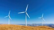 © Kasitthanin - A scenic view of wind turbines on a sunny day with blue sky and rolling hills, symbolizing renewable energy and sustainability.
