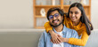 © Prostock-studio - A young Indian couple shares a cheerful embrace on a comfortable sofa, showcasing their affection. The inviting indoor environment and joyful expressions highlight their connection.