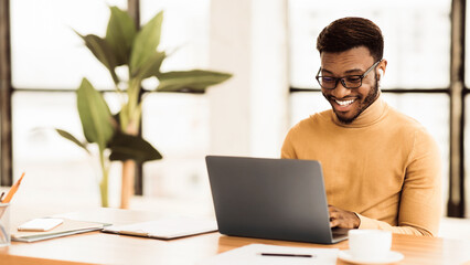 Wall Mural - Male Executive. Happy black businessman using laptop, listening to music in wireless headphones, copyspace, panorama