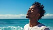© marwan - A young man with dreadlocks enjoys the warm summer breeze with his eyes closed, standing on a beach with the ocean in the background.