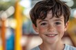 © DenisNata - Portrait of a young boy with dark hair and freckles, smiling outdoors with a colorful background.