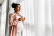 © Maria Vitkovska - Pregnant woman drinking coffee by the window and enjoying sunlight
