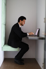 Wall Mural - A man in a suit is sitting at a desk with a laptop. He is typing on the laptop and he is focused on his work. Concept of professionalism and productivity, as the man is dressed in a suit