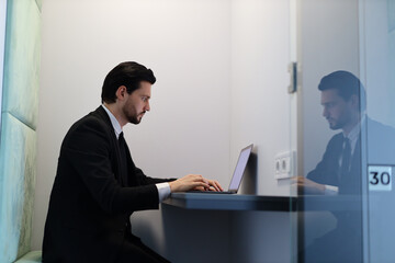 Wall Mural - A man in a suit is typing on a laptop in a cubicle. The cubicle is numbered 30