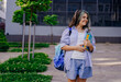 © Iryna - A teenage girl smiling looks away, walking to school dressed in a backpack, carrying notebooks