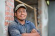 © Joaquin Corbalan - A Mexican bricklayer stands confidently with arms crossed, showcasing his skills at a construction site in mid-afternoon light