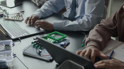 Cropped shot of unrecognizable Black male teacher and gen z student sitting at desk and typing code on laptop keyboards during programming lesson in classroom