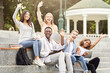 © Prostock-studio - Happy friends international students waving at camera while studying with laptop in city, sitting on stairs, empty space