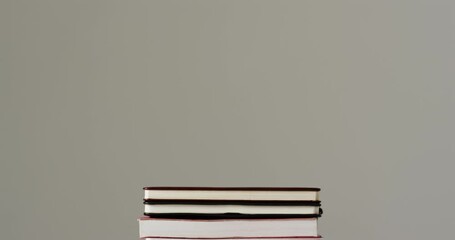 Sticker - A stack of various hardcover and paperback books sits against a neutral background, with copy space