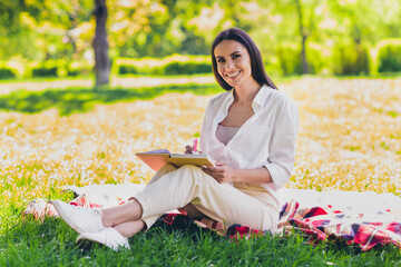 Sticker - Full size photo of attractive young cheerful girl sit picnic blanket write notebook wear white garment having fun outside outdoors