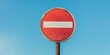 © kiimoshi - A weathered red no entry sign against a clear blue sky, symbolizing restriction and prohibition in an urban environment.