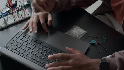 From above shot of two unrecognizable gen z schoolboys using laptop while preparing electronics project together at desk in classroom, working with circuit board details and wires