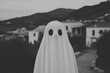 © neiros - During the Halloween holiday, an unrecognizable kid in a white ghost costume is seen having fun on the street and looking at the camera