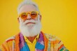 © W. Thienthongthai - Elderly man with a white beard wearing a colorful outfit and yellow-tinted glasses against a yellow background.