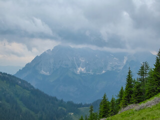 Hiking trail along alpine meadow with panoramic view of cloud covered mountain peaks in Eisenerz Alps, Styria, Austria. Tranquil atmosphere in Austrian Alps in spring. Outdoor trip on overcast day