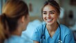 © TheGoldTiger - Smiling healthcare professional in scrubs and a stethoscope talks with another person, likely a colleague, in a medical setting