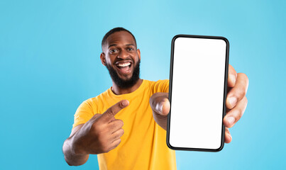 Wall Mural - mobile advertisement. overjoyed black man pointing at cellphone with empty white screen on blue stud