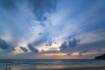 Wall Mural - A stunning sunset over the ocean with soft golden light reflecting on the water, featuring silhouettes of people walking along the shore. Water flows from a small stream into the sea.