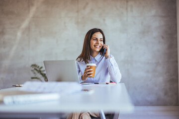 Smiling Businesswoman Enjoying Coffee While Taking Phone Call