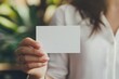 © SKIMP Art - Close-up photo of a woman's hand holding a blank business card, wearing a white-colored shirt, with a blurred background Generative AI