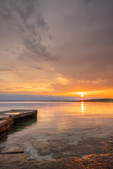 Wall Mural - Beach in the morning. Sunrise, pebble beach on a rocky coast. The sky is reflected in the water of a bay. Natural spectacle of a Mediterranean landscape, island of Vir, Zadar, Dalmatia, Croatia, Adria