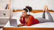 © Prostock-studio - African American Girl In Headphones Using Laptop Watching Movie Relaxing On Weekend Lying On Bed At Home. Selective Focus