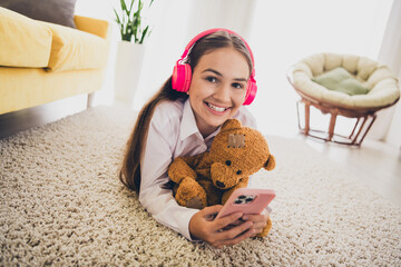 Poster - Full length photo of cute teen girl lying floor headphones device teddy bear wear uniform remote lesson education from home indoors